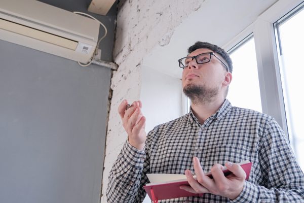 Homeowner checking an indoor heat pump unit while troubleshooting cooling problems and HVAC performance.